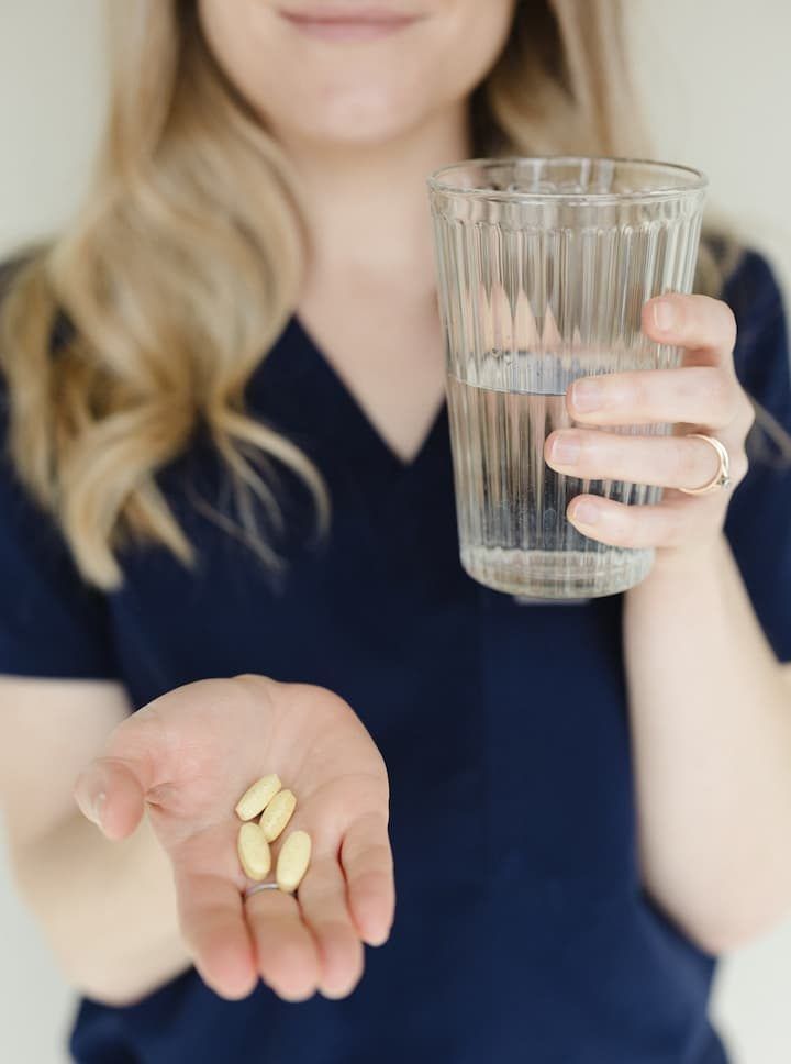 a woman holding a glass of water and a handful of pills