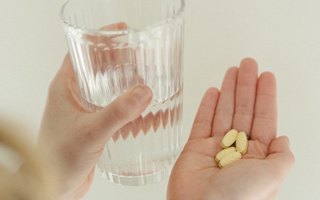 a hand holding pills and a glass of water
